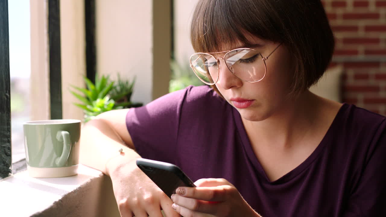 mujer joven usando teléfono inteligente por la ventana