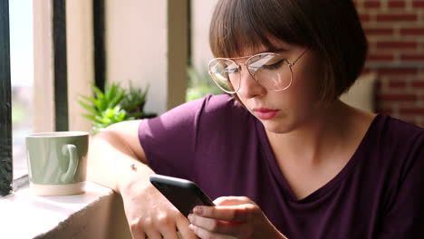 young woman using smartphone by window