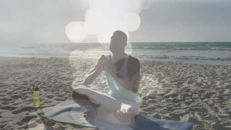 animación de luces brillantes sobre un hombre afroamericano haciendo meditación de yoga en la playa