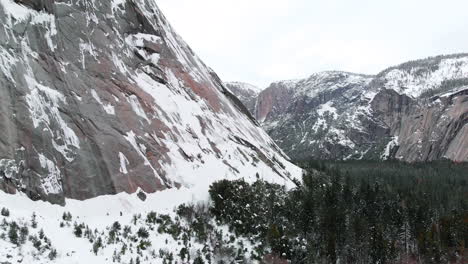 Aerial-drone-footage-slowly-flying-past-snowy-granite-cliffs-towering-over-Yosemite-valley-in-winter