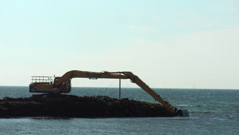 hydraulic excavator dredging silt from ocean bay coastline, slow motion