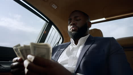 Closeup-african-man-counting-money-at-car.-Businessman-sitting-with-money-at-car