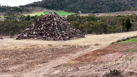 a dry stone pyramid stands in an open grassy field as the camera smoothly pans sideways, revealing the rural australian landscape under soft daylight