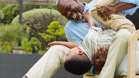 grandfather having fun playing with grandson in garden holding him upside down