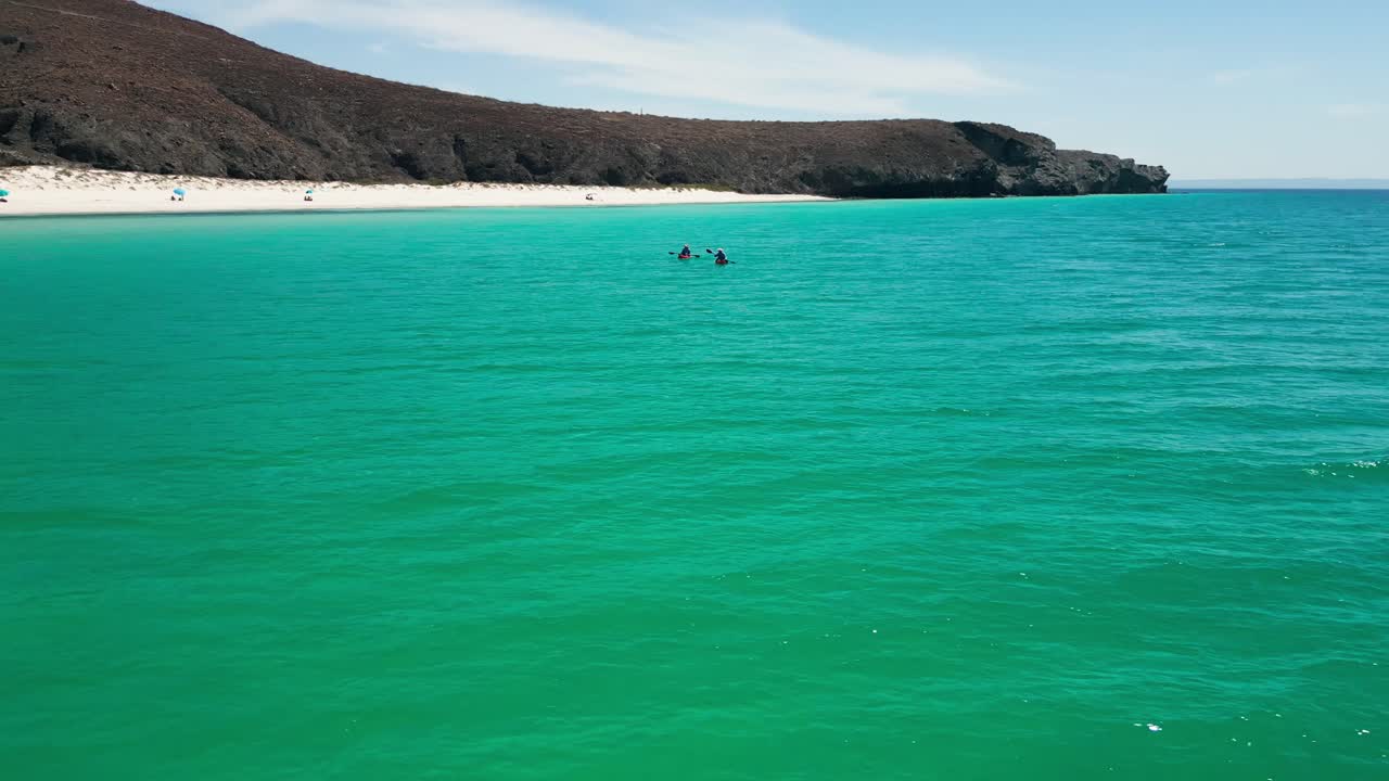 Emerald waters with two kayakers gliding through the calm bay, surrounded by hills