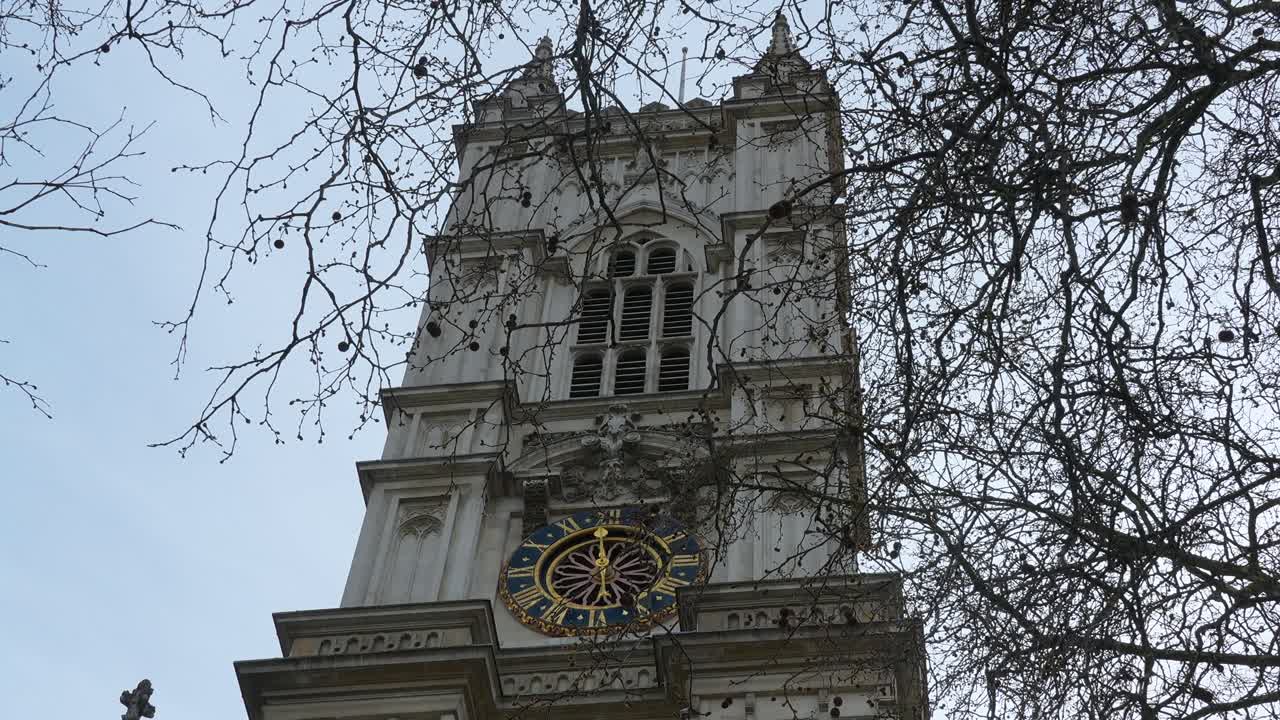 St Margaret’s Church clock tower in London with tree branches in the foreground. Daytime view showing church facade and clock detail