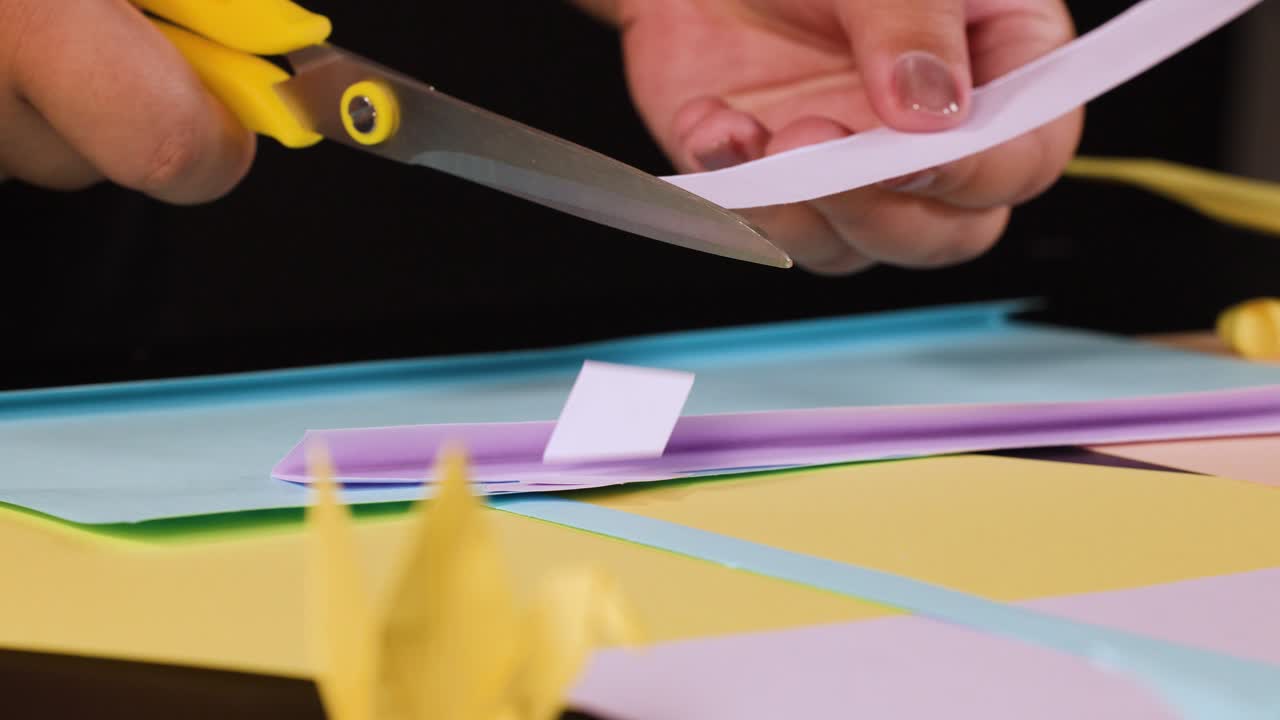 Primo piano di mani che usano forbici gialle per tagliare carta rosa su una scrivania colorata