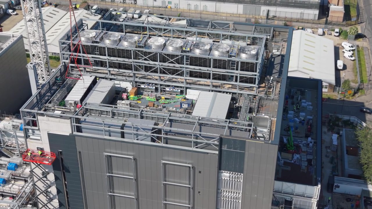 Luftfoto af en stor moderne datacenterbygning under opførelse om dagen. Arbejdere og udstyr er synlige, mens infrastrukturen udvides i et industriområde