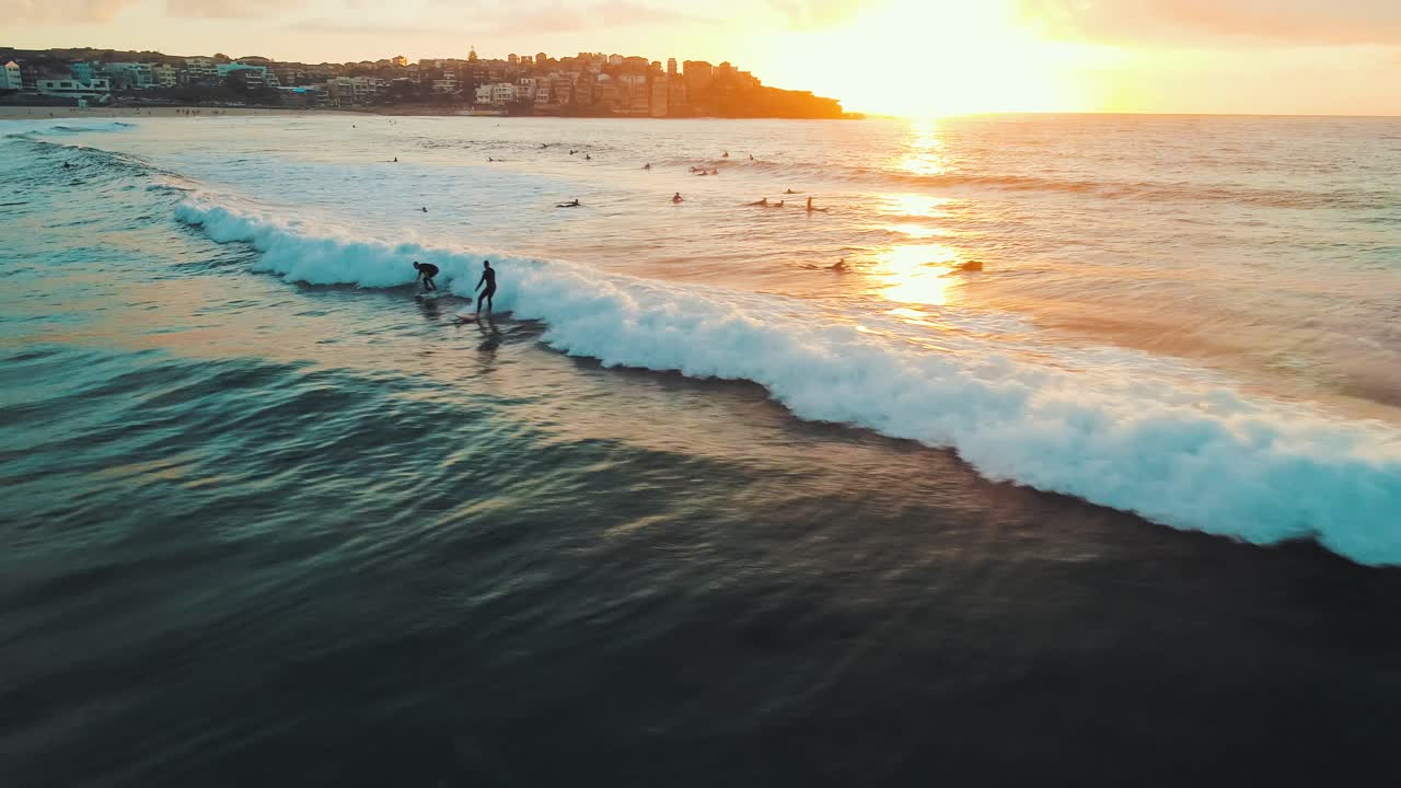 Ripresa aerea dinamica di un surfista che cavalca un'onda a Bondi Beach all'alba