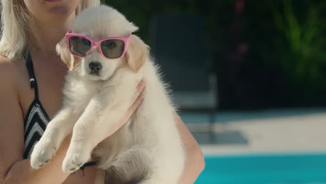 Eine-Frau-Im-Bikini-Hält-Einen-Blonden-Welpen-Mit-Sonnenbrille-Im-Arm.-Sommer-Und-Urlaub-Mit-Einem-Haustierkonzept