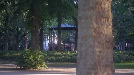 Beautiful-gazebo-in-a-stunning-park-in-the-city-of-Brussels,-Belgium,-at-the-Koekelberg-district,-with-tall-green-summer-trees-and-scenery-surrounding-it-and-houses-in-the-far-background