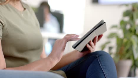 midsection of caucasian casual businesswoman using tablet in office, slow motion