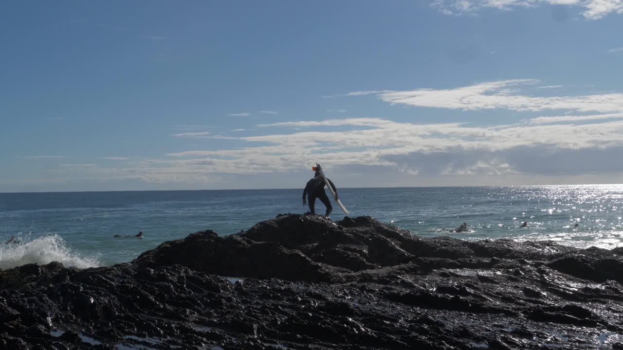 surfista con tabla de surf en la roca salta a la ola del océano en rocas de pargo - surf en la playa en la costa de oro, australia - amplia toma en cámara lenta