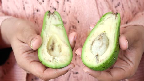 woman holding two halves of an avocado