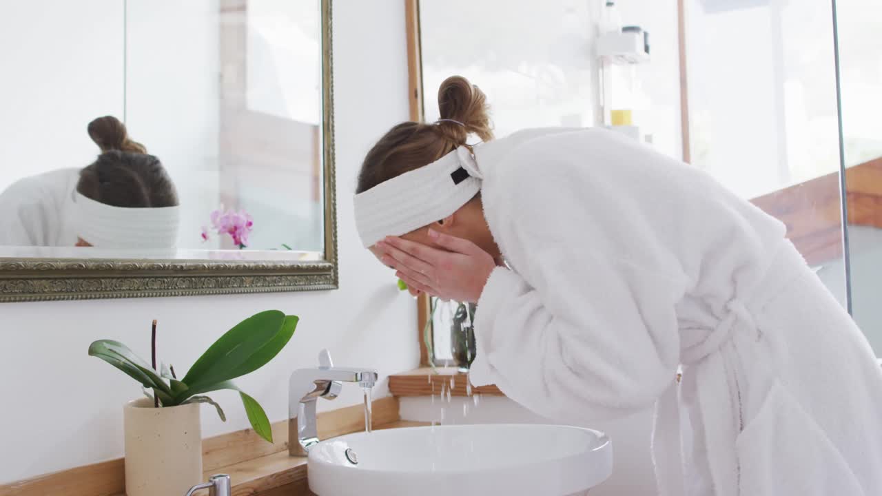 Woman in bathrobe washing her face in the sink