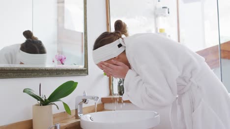 woman in bathrobe washing her face in the sink