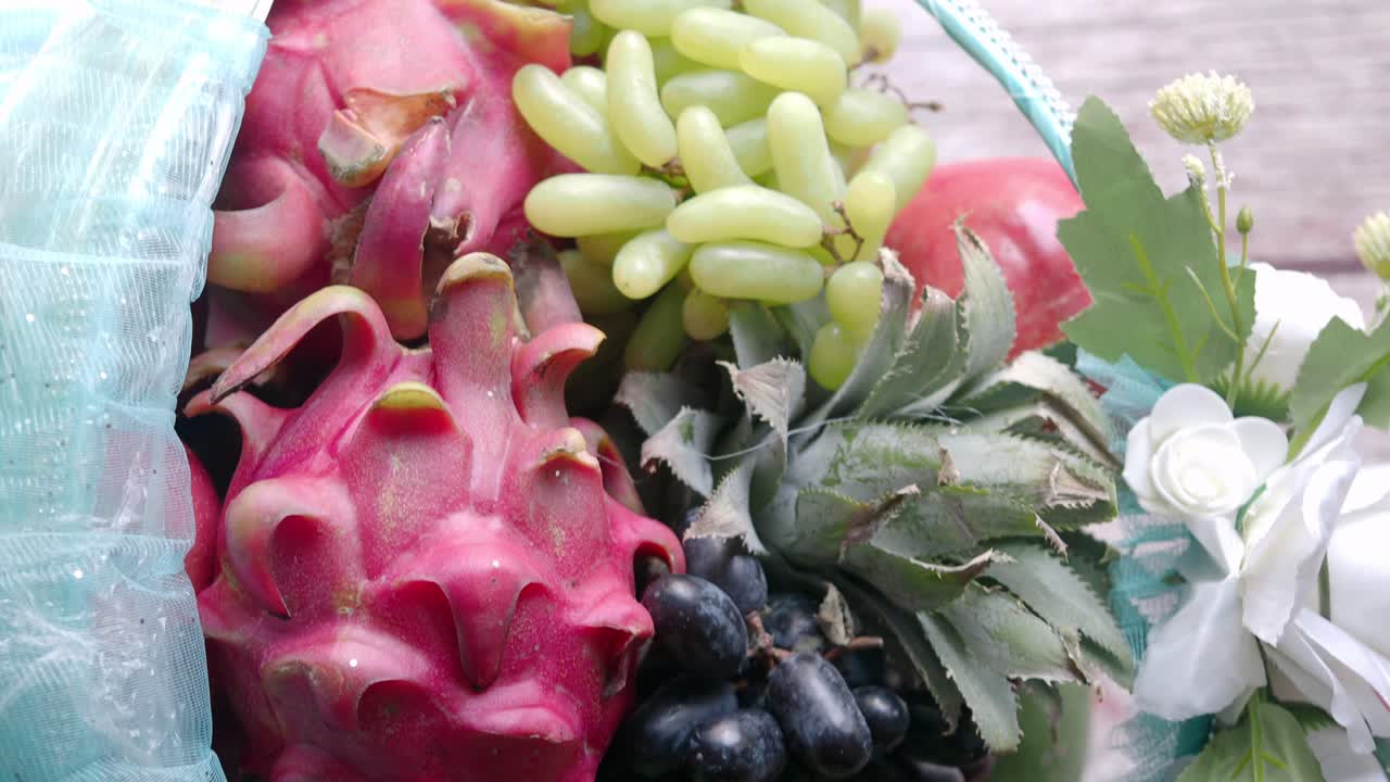 A fruit basket with dragon fruit, grapes, pineapple, and flowers
