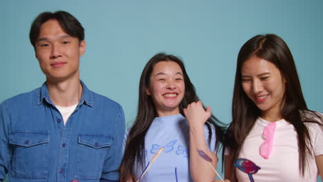 group of young friends in front of blue studio background having fun posing for photo booth style portraits with props