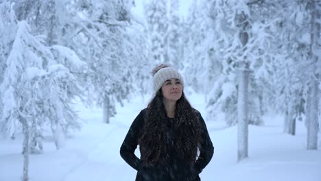 girl looking around with snowflakes falling on her in snowy winter wonderland in lapland, finland, arctic circle