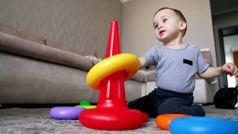 beautiful caucasian kid building pyramid. happy baby boy playing at home. black cat at backdrop. low angle view.