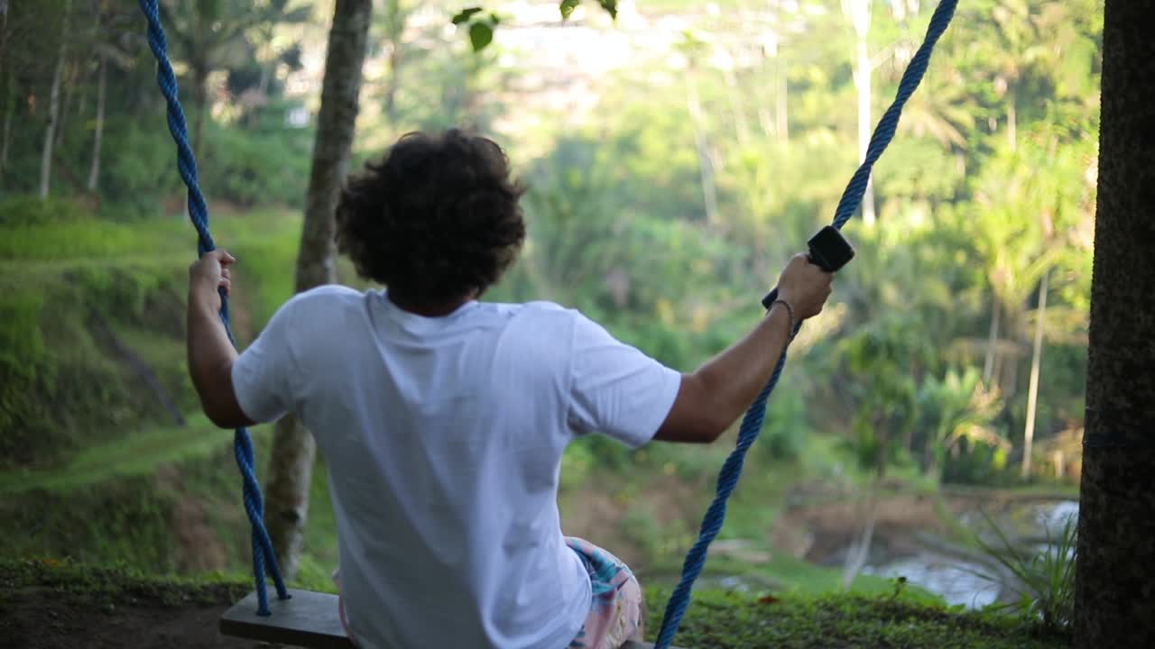toma en cámara lenta de un turista caucásico masculino balanceándose en un columpio sobre los arrozales en las terrazas de arroz tegallalang en bali, indonesia