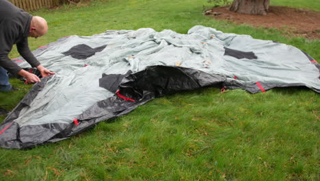 a mature man laying out a tent ground sheet on the grass in a field whist camping at a campsite