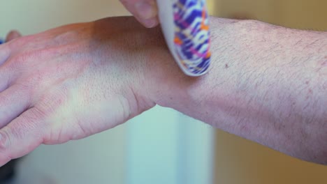 little handheld electric razor white with purple and orange design pattern, shaving the hand and wrist of white caucasian man or women