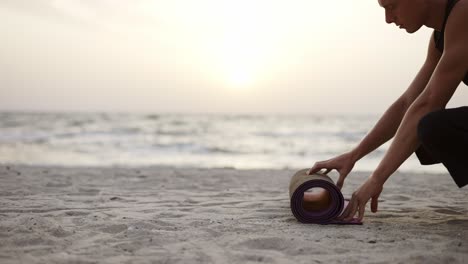 A-young-man-lays-out-a-sports-mat-and-prepares-for-a-yoga-class-during-the-dawn-of-the-son.-Leisure-time,-recreation