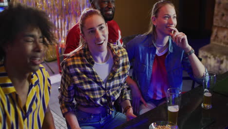 video of diverse group of happy friends drinking and reacting to sports game on tv at a bar