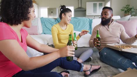 three diverse happy female and male friends talking, with beer and pizza at home, in slow motion