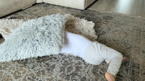 lovely baby boy in white shirt lies on the floor with pacifier in mouth. child cuddles with a soft fluffy pillow. top view.