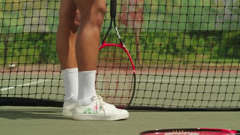 a girl bounce a tennis ball at her feet on a tennis court on a sunny day