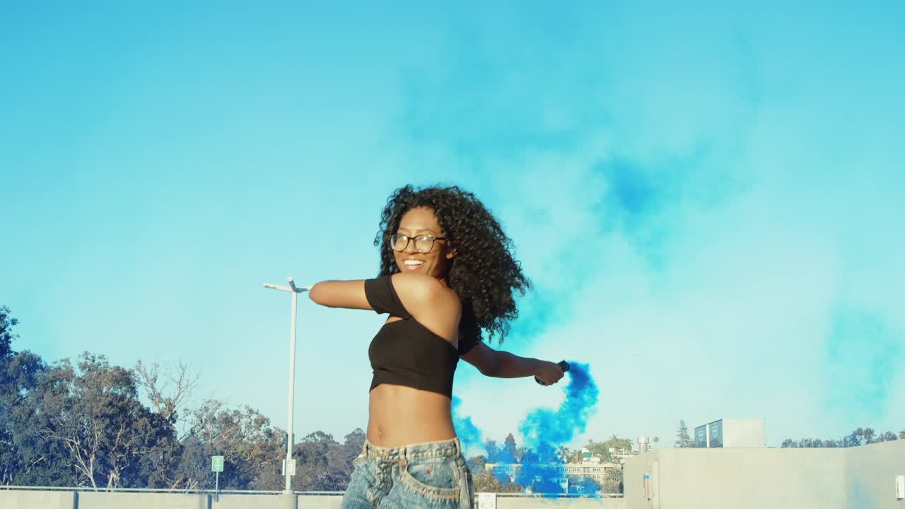 Young woman dancing outside with smoke grenade at sunset on rooftop parking garage