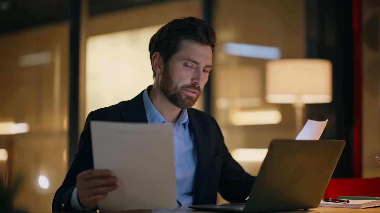 Night manager analyzing papers at dark laptop workplace closeup. Successful man