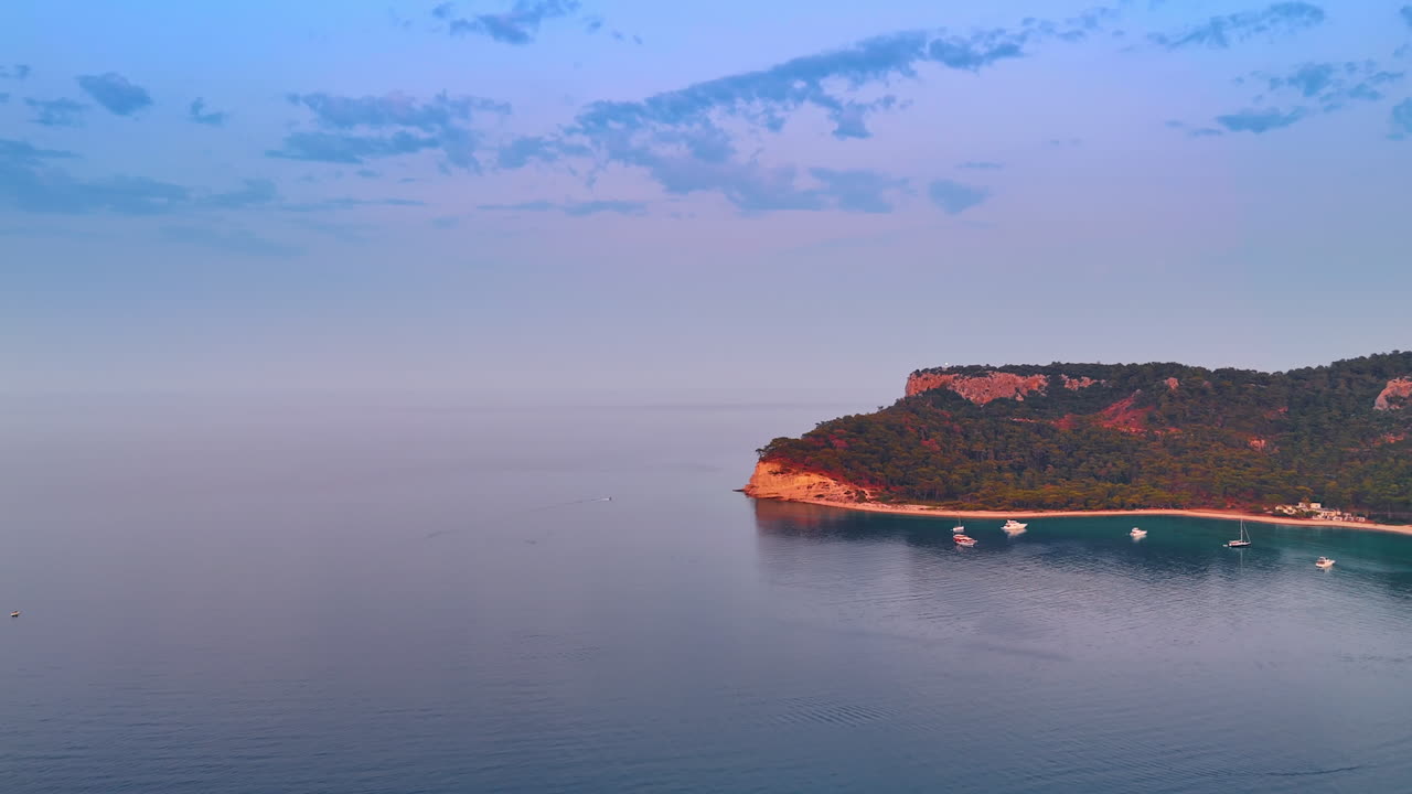 Sunset over calm waters at coastal cliff. A serene sunset paints the sky, casting colors over the quiet sea near a rugged coastal cliff with boats drifting