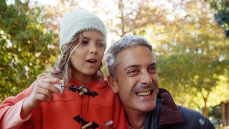 chica soplando burbujas sostenida por papá al aire libre
