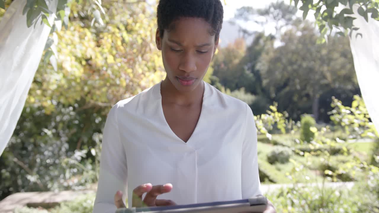 Portrait of happy african american female wedding officiant holding tablet in garden, slow motion
