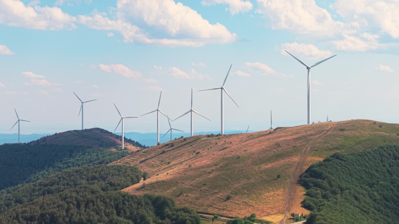 Wide view of wind turbines spinning gracefully atop green mountain ridges in central Bulgaria. Clean, renewable energy set against a stunning sky