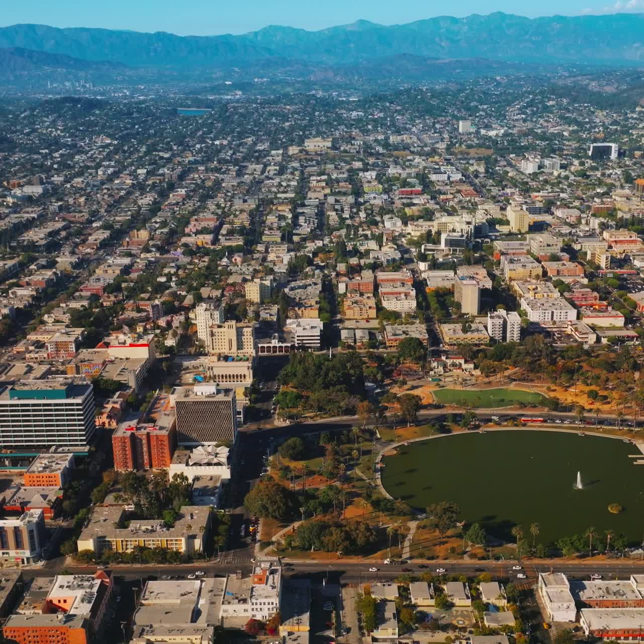 Lovely park with a pond in the middle in the urban panorama. Densely built Los Angeles cityscape at the backdrop of California mountains