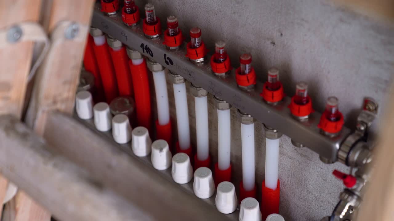 Underfloor heating manifold with red and white pipes mounted on concrete wall