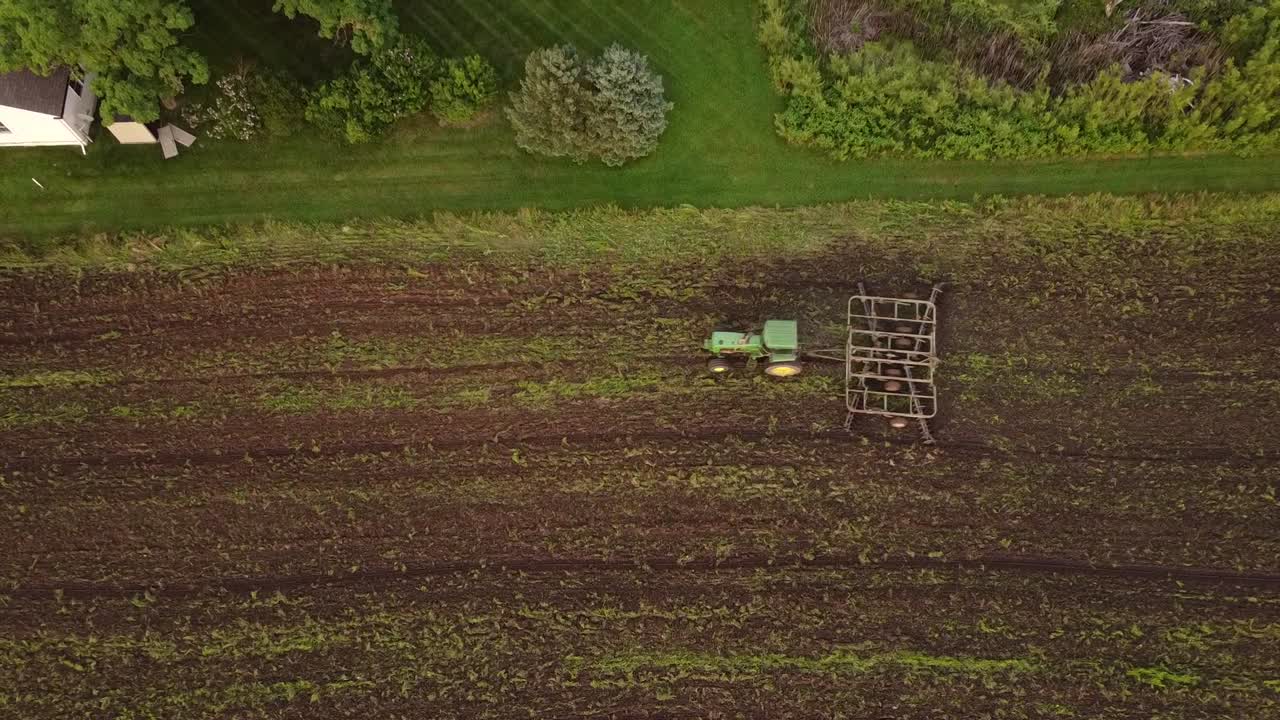 Top-down View Of An Agricultural Tractor Tilling The Vast Field For Planting New Crops In Monroe County, Michigan - ascending drone shot