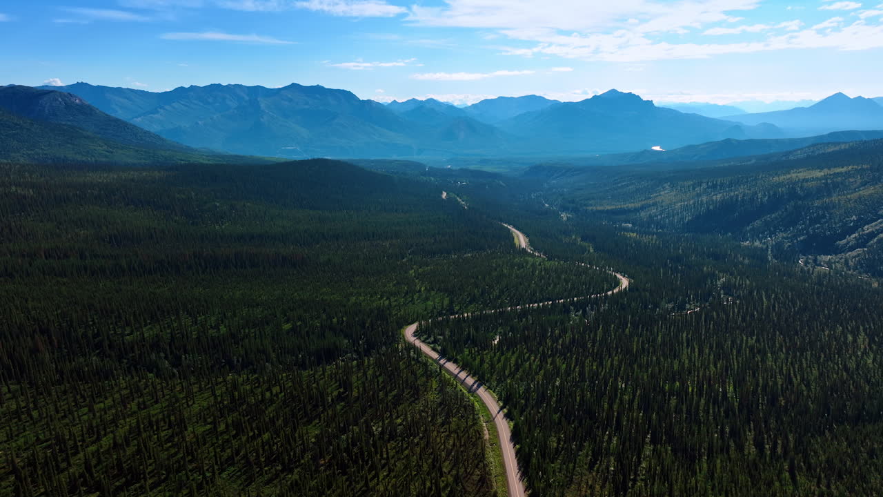 Stunning Alaskan wilderness. Vast green forests stretch across the landscape, met by towering mountains under a clear blue sky