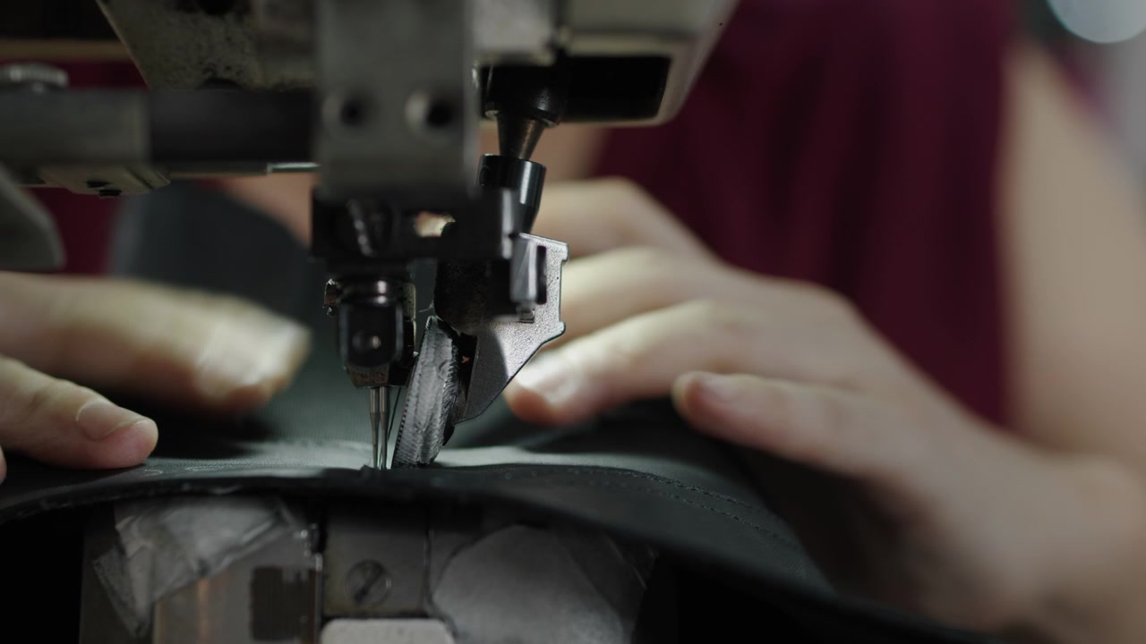Hands sewing leather material with industrial machine in shoe production process