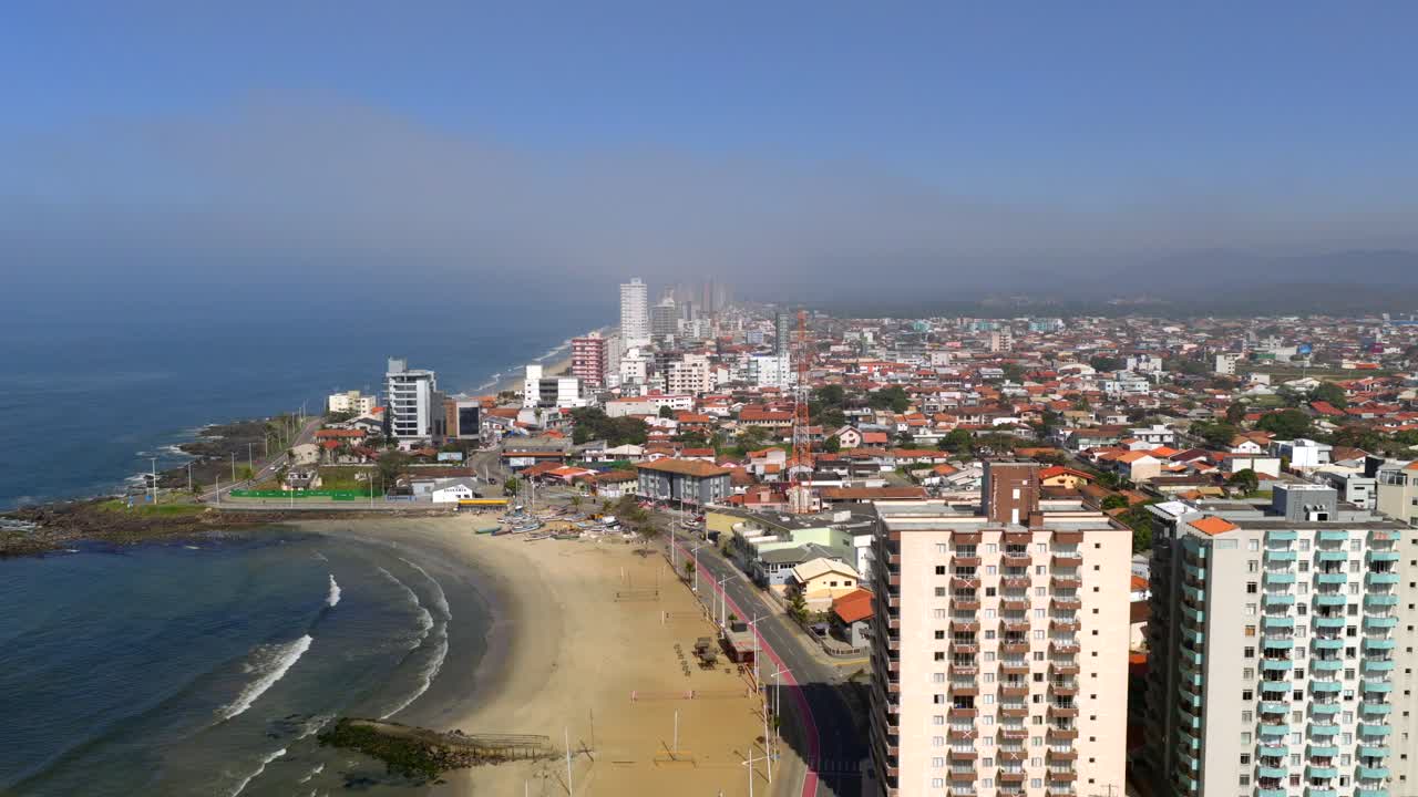 Aerial perspective revealing Barra Velha coastal cityscape, modern structures lining sandy shoreline, merging with sparkling Atlantic waters under vibrant blue sky