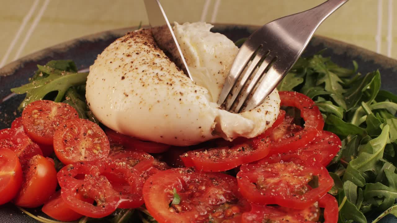 Burrata or Mozzarella cheese on fresh tomatoes and green arugula on plate close-up. From Italian cow's milk cheese made from mozzarella and cream.The outer casing is solid cheese, while the inside contains stracciatella and clotted cream, giving it an unusual, soft texture.
