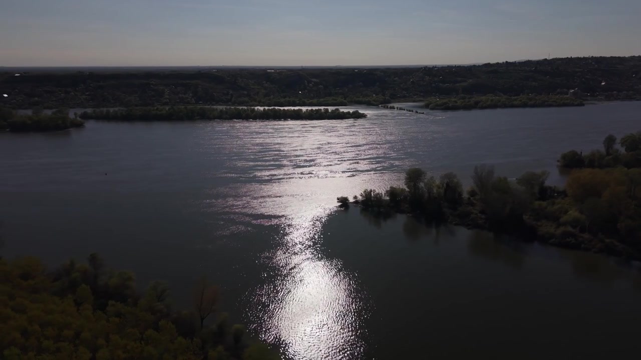 Veduta aerea con drone della confluenza dove si incontrano i fiumi Danubio e Tibisco. Rive boscose, acque ampie e calme e campi agricoli di un giallo brillante sullo sfondo sotto un cielo azzurro e limpido.