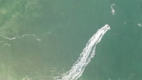 a boat leaving a wake on the turquoise waters off the coast of nazaré, portugal, aerial view