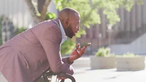 Hombre-Afroamericano-En-La-Ciudad-Con-Bicicleta-Parada-Al-Sol-Usando-Un-Teléfono-Inteligente