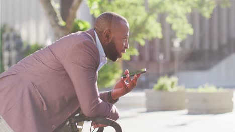 african american man in city with bike standing in the sun using smartphone