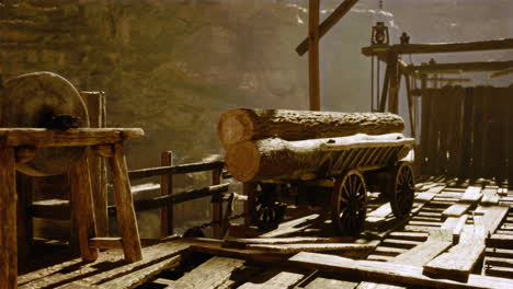 a vintage wood mill with a grinding stone and a wooden cart with logs.